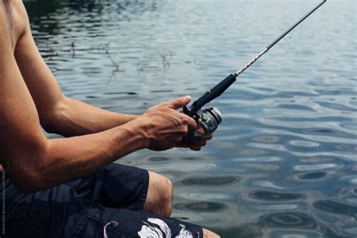 He is holding a fishing rod in one hand and a fish by its mouth is another.
